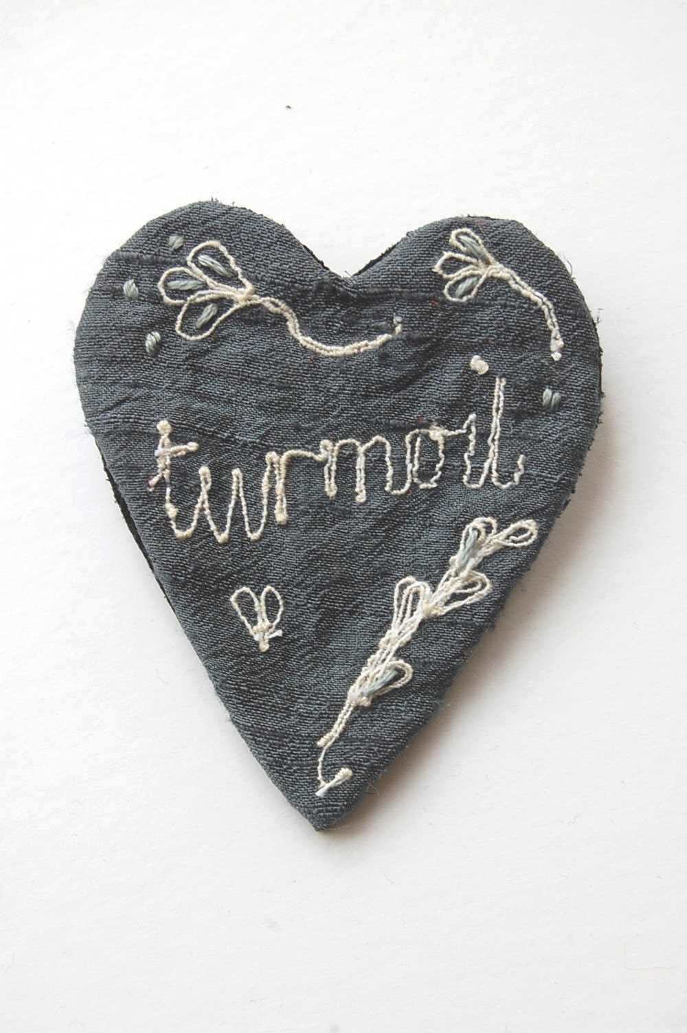 Brooch embroidered silk with the word 'turmoil'