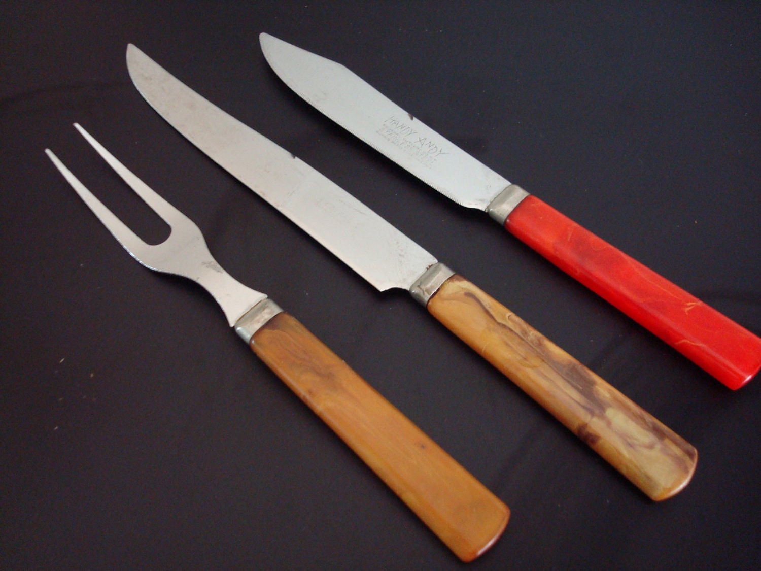 Three vintage bakelite handle utensils- 1 serving fork and two knives.  Stainless steel metal.