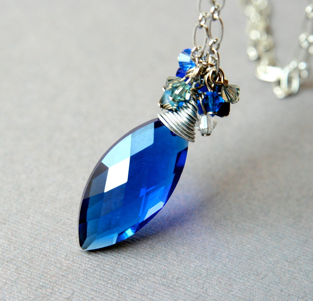 Royal Blue Crystal Pendant  on a metallic long chain with a cluster of crystals scattered around a large oval faceted glass drop
