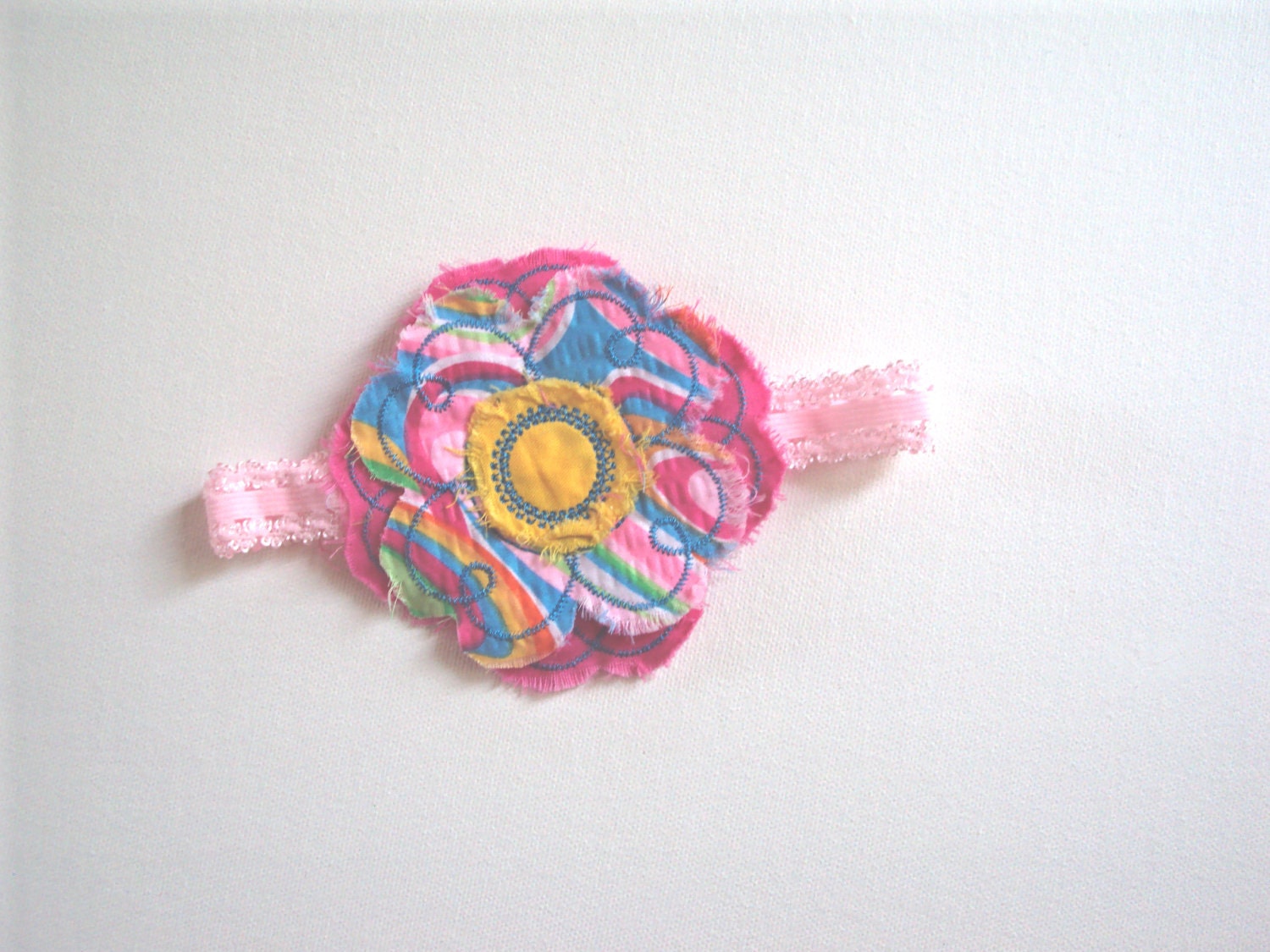 Frayed shabby flower in pinks, teal blue and yellow is attached to a headband.