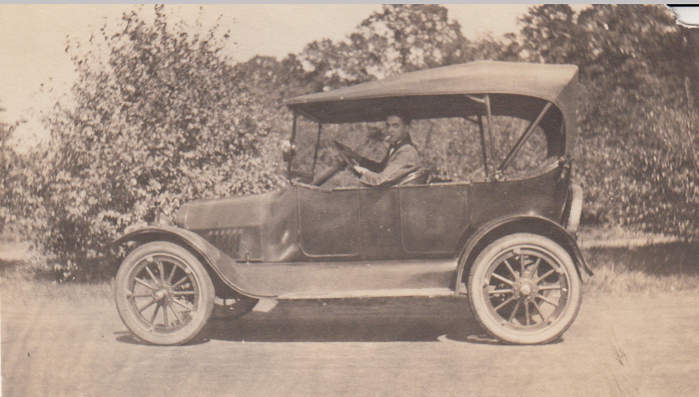 Vintage/ Antique photo of a man driving a vinatge and smoking a cigarette