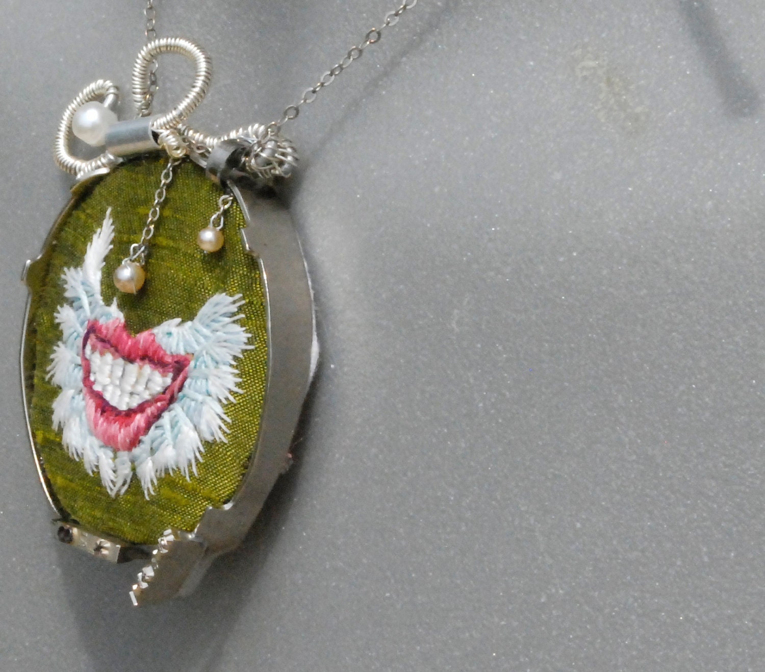 Green embroidered necklace of a mightily winged smile wrapped in typewriter keys "Pneumothorax"