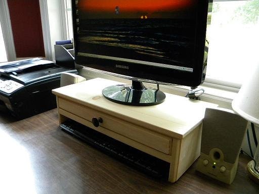 Computer monitor stand with drawer for extra storage and hidden hole in drawer back for cell phone chargers