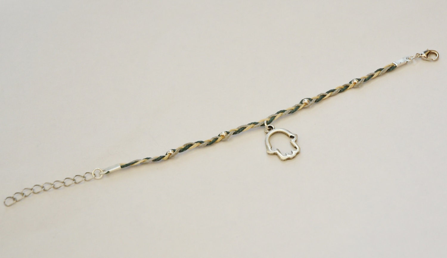 Braided Hamsa Bracelet- braided bracelet with a silver plated hamsa charm and 3 cords: gray, blue, beige. Decorated with silver plated beads
