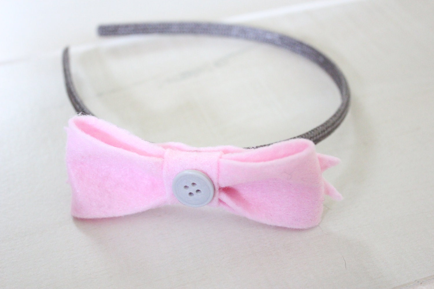 Pink felt bow with grey button on a grey headband
