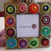 Square woden frame decorated with layered colorful felt rounded pieces, bottle tops and brass pins