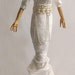 A gourd doll in white velveteen and chain on a wood base