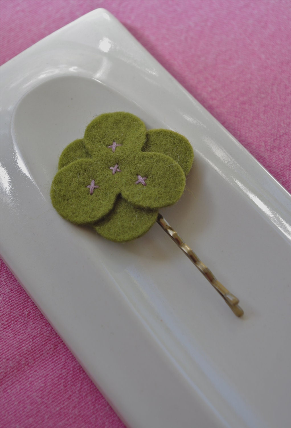 Green wool felt flower hair clip with lilac stitching.