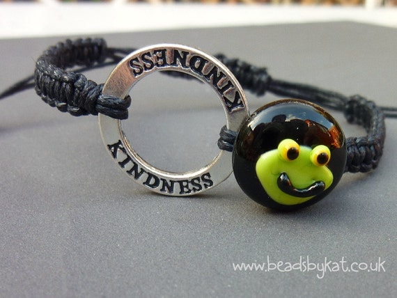 This is a little black button with a frog's face on it, for Team Jaxon F.R.O.G, on macrame'd cotton. The silver coloured affirmation ring says 'Kindness' which is what this is all about