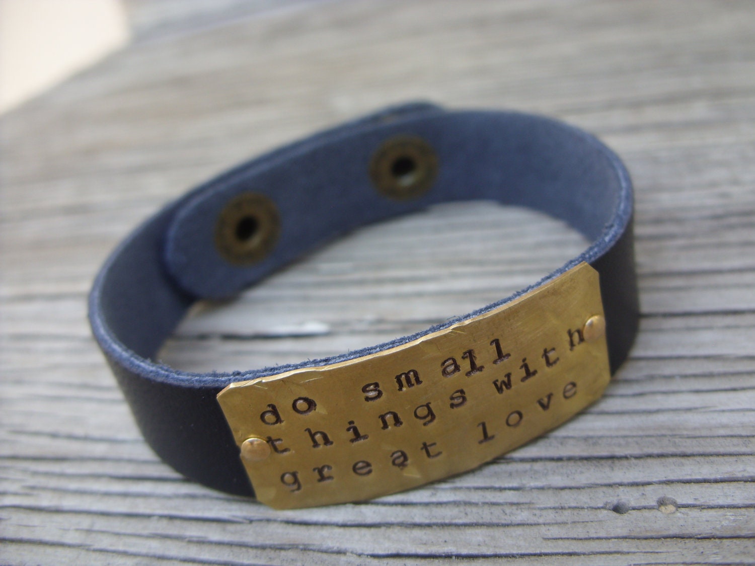 A riveted, brown leather cuff bracelet with hand stamped brass do small things with great love- distressed and embellished wording