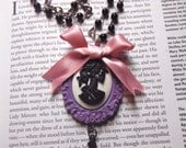 Skeleton Lady cameo in purple frame with cross charm and pink bow.