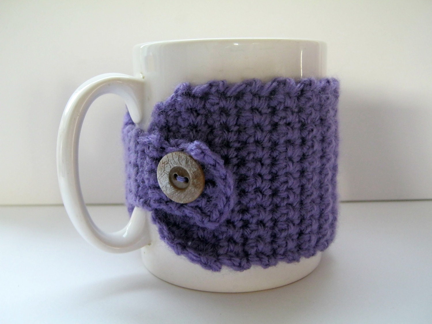 Crocheted mug cosy in purple with silvered wood-effect button