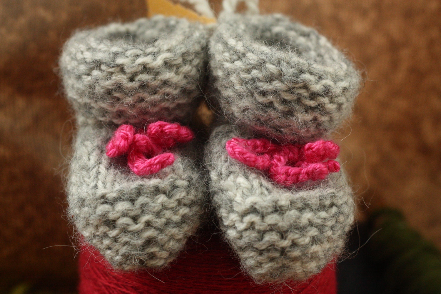 Hand knitted baby booties in fuzzy grey marled yarn with pink hand hand crochet ties. Size 0-3 months.