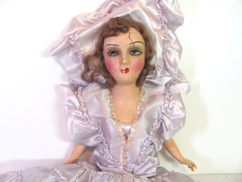 Vintage antique composition doll in a purple dress for display