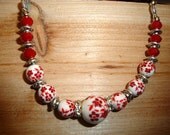 Hand painted red flowers on white glass beads accent this necklace perfectly