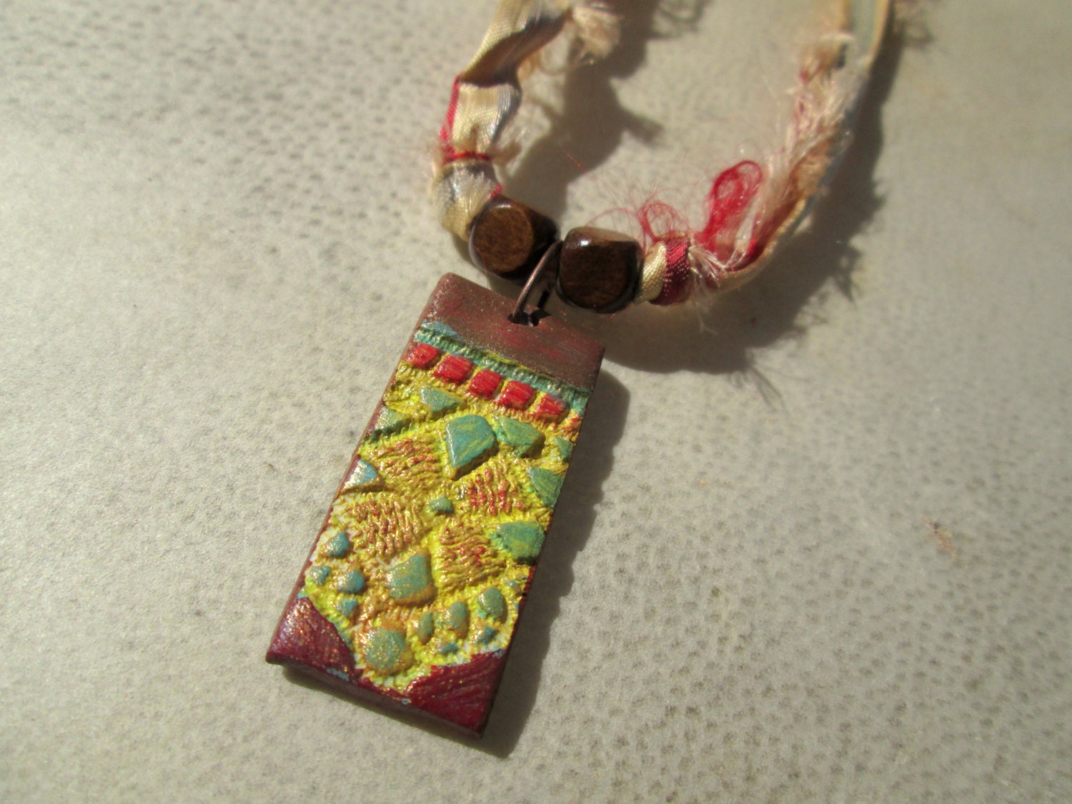 Frida. Hand-Painted Lace Textured Polymer Clay Pendant on Recycled Sari Silk Ribbon. Brown Wooden Beads. Yellow, Red, Green, Tan.