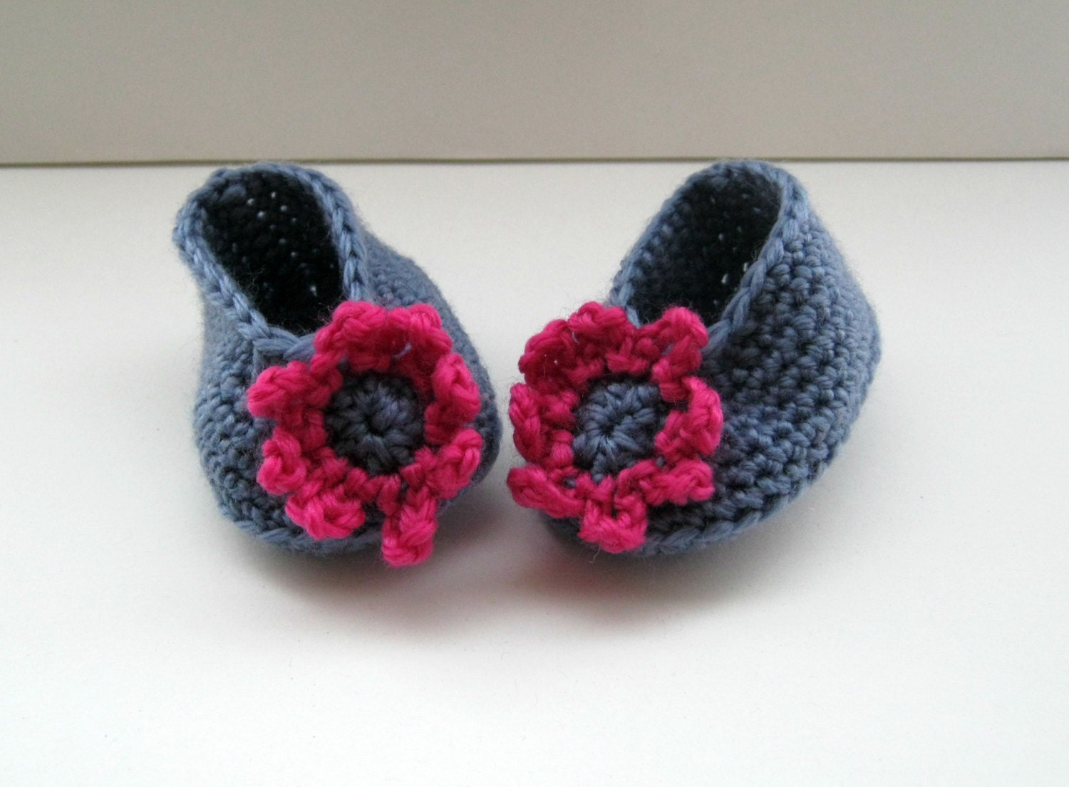 Crocheted baby booties in mid blue with a deep pink and blue flower