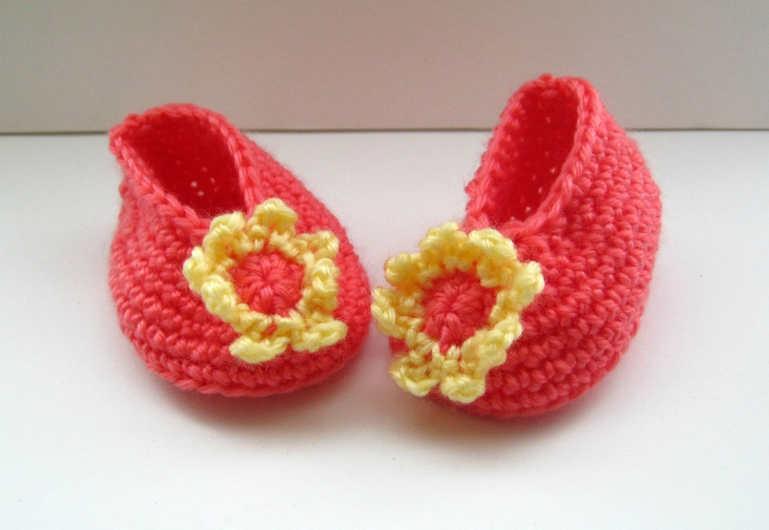 Crocheted baby booties in deep peach with a yellow and peach flower