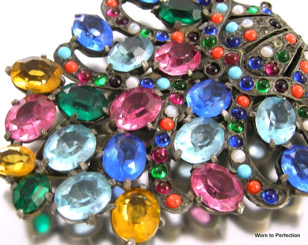A rare Eisenberg Original dress clip. A popular Eisenberg design, the multi-color rhinestones are what makes this dress clip rare. I shared a photo of this clip with an Eisenberg expert and they had never seen this design with the multi-colored stones. I want to use the word massive to describe this Eisenberg. The dress clip measures 2-7/8 x 2-5/8 inches, which doesn't sound massive but to hold this in your hand, it's amazing. All stones are present. The clip is signed Eisenberg Original on the back. It's a chance to own something truly special.