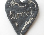 Brooch embroidered silk with the word 'turmoil'