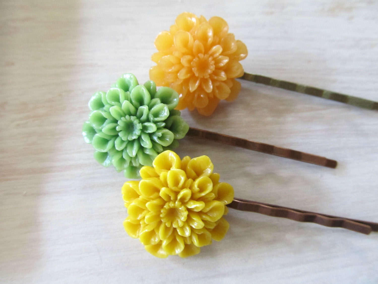 A trio of floral bobby pins in mustard, tangerine and grass green