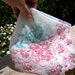 Handkerchief has scalloped edge, pink carnations, roses, teal ribbon, sheer white. Wedding gift idea for mother of the bride or groom.