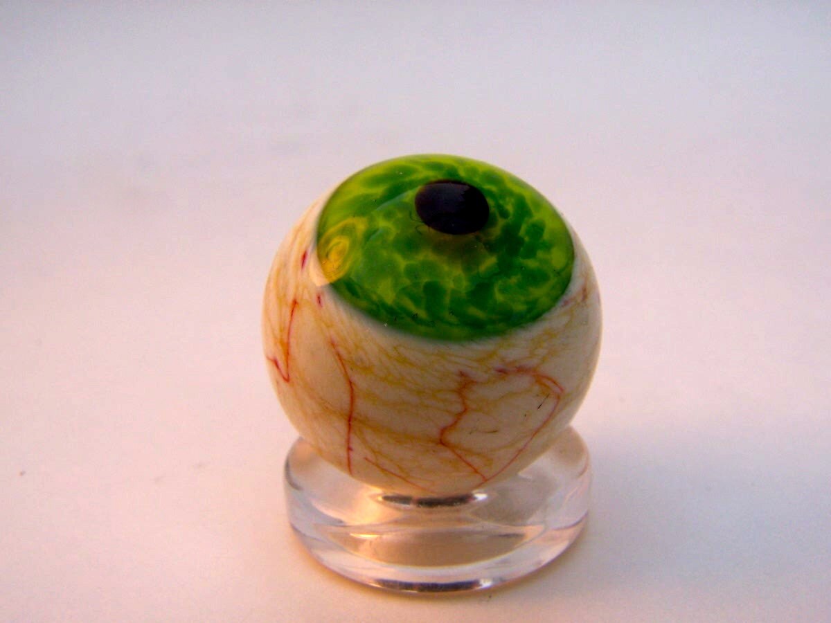 Unique lampwork glass eye marble with green translucent iris.