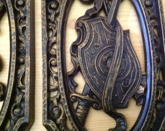 pair of Homco 1974 wall hangings featuring Spanish sword/ shield and sceptor/arrows in black and gold