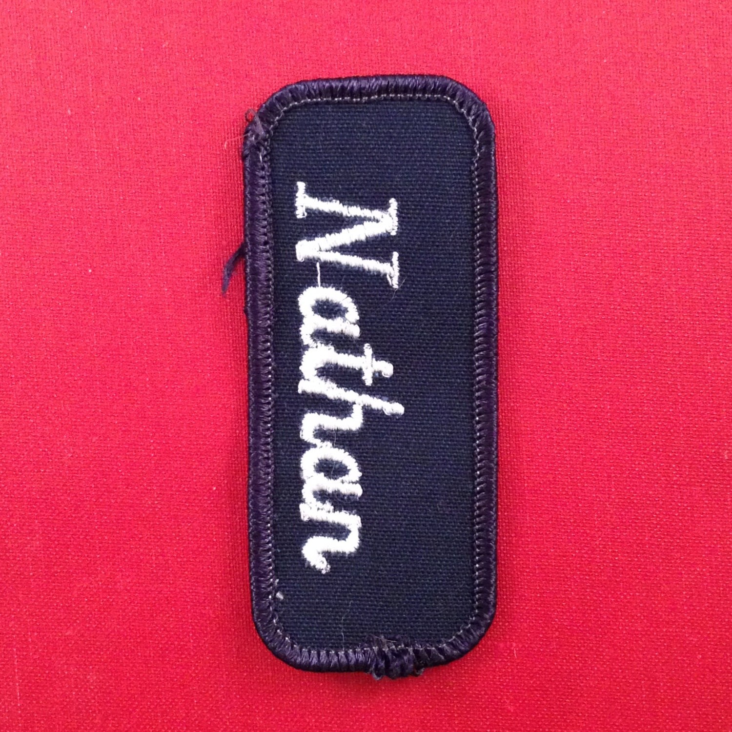 Nathan. A navy blue work shirt patch that says