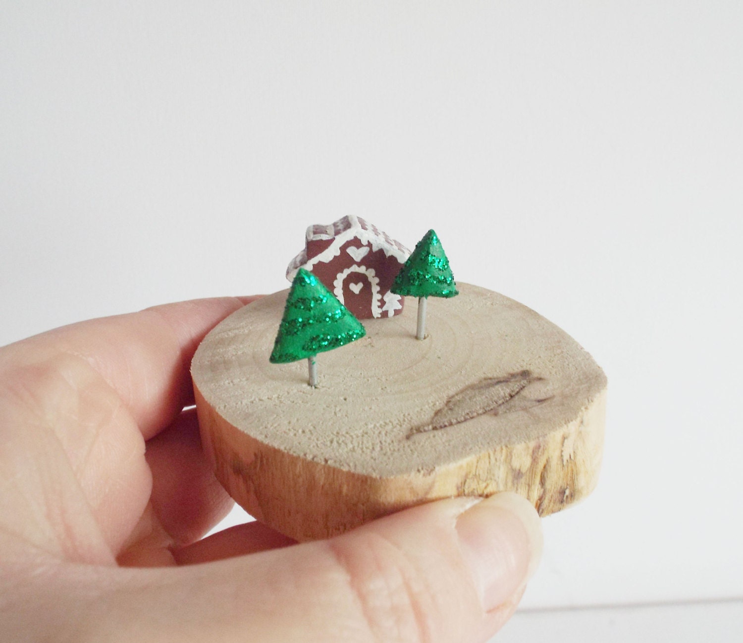 Miniature handmade clay gingerbread house with sparkly clay christmas trees attached on slice of wood christmas decoration.