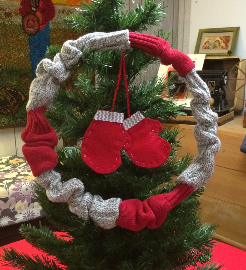 Christmas wreath upcycled from sweater sleeves. Red and gray sweater sleeves cover an embroidery hoop. Red felt mittins hang from middle