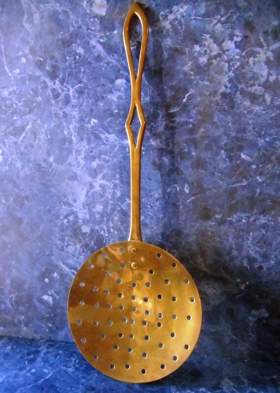 Vintage brass strainer spoon with decorative handle.
