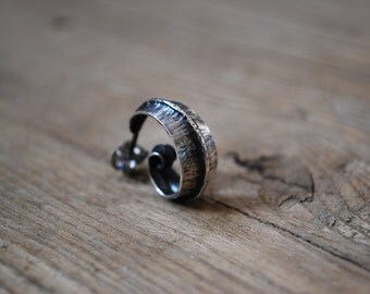 Une boucle d'oreille solitaire forgée en argent massif patiné pour homme ou femme