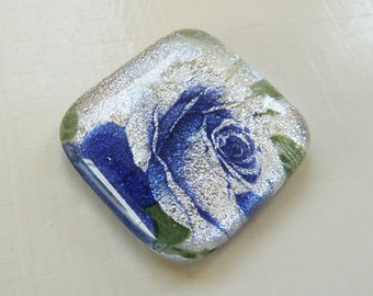 Fused glass cabochon on silver dichroic glass with purple blue rose image.