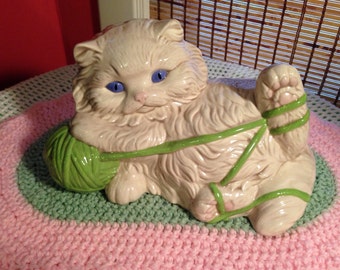 Large vintage white kitty playing with a green yarn ball.