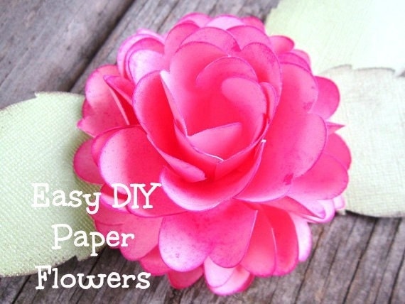 A blooming paper rose on paper leaves lays on a wooden table. The text in the left lower corner reads, "Easy DIY Paper Flowers." 