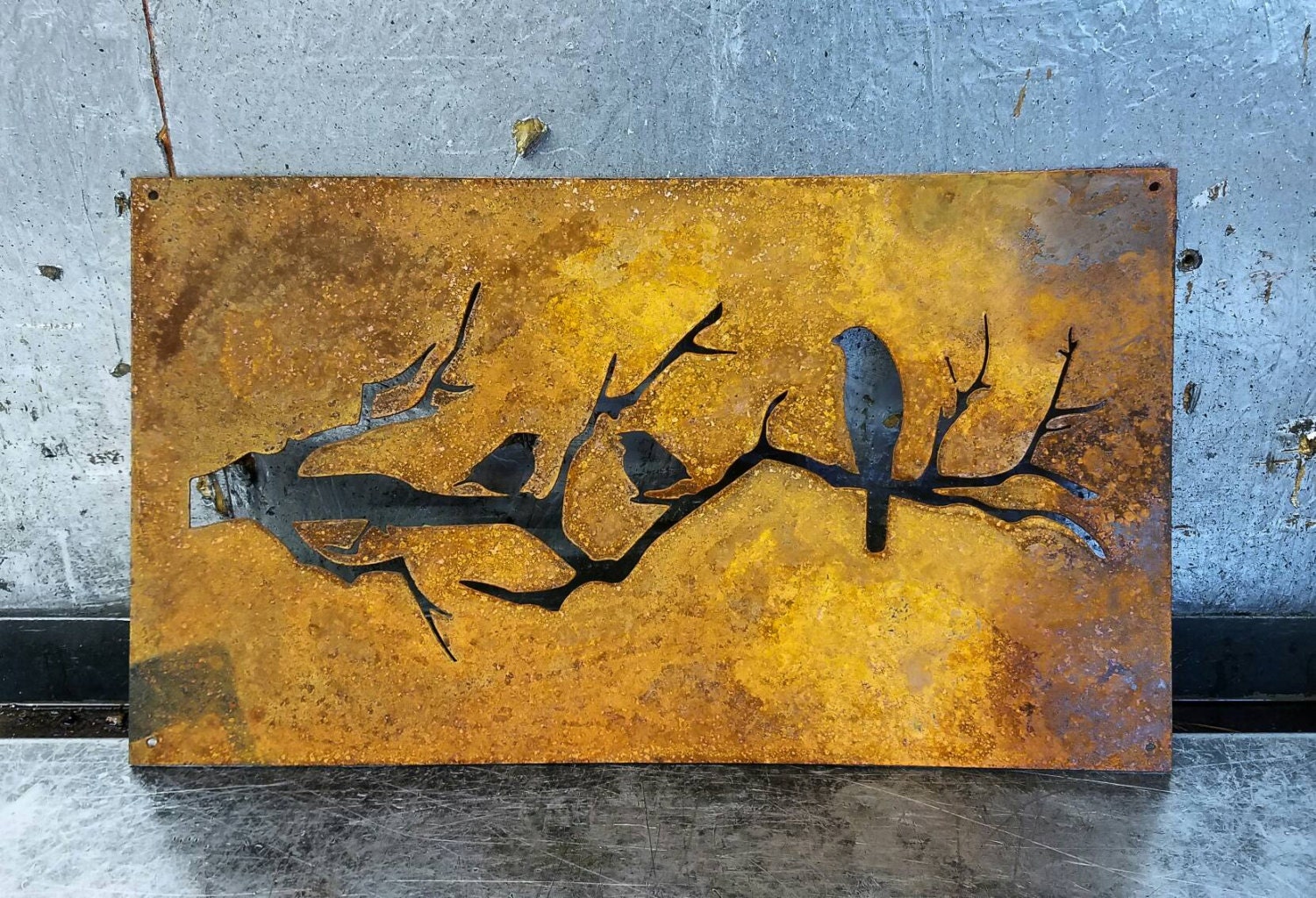 Birds on a branch silhouette cut out of a sheet of metal.