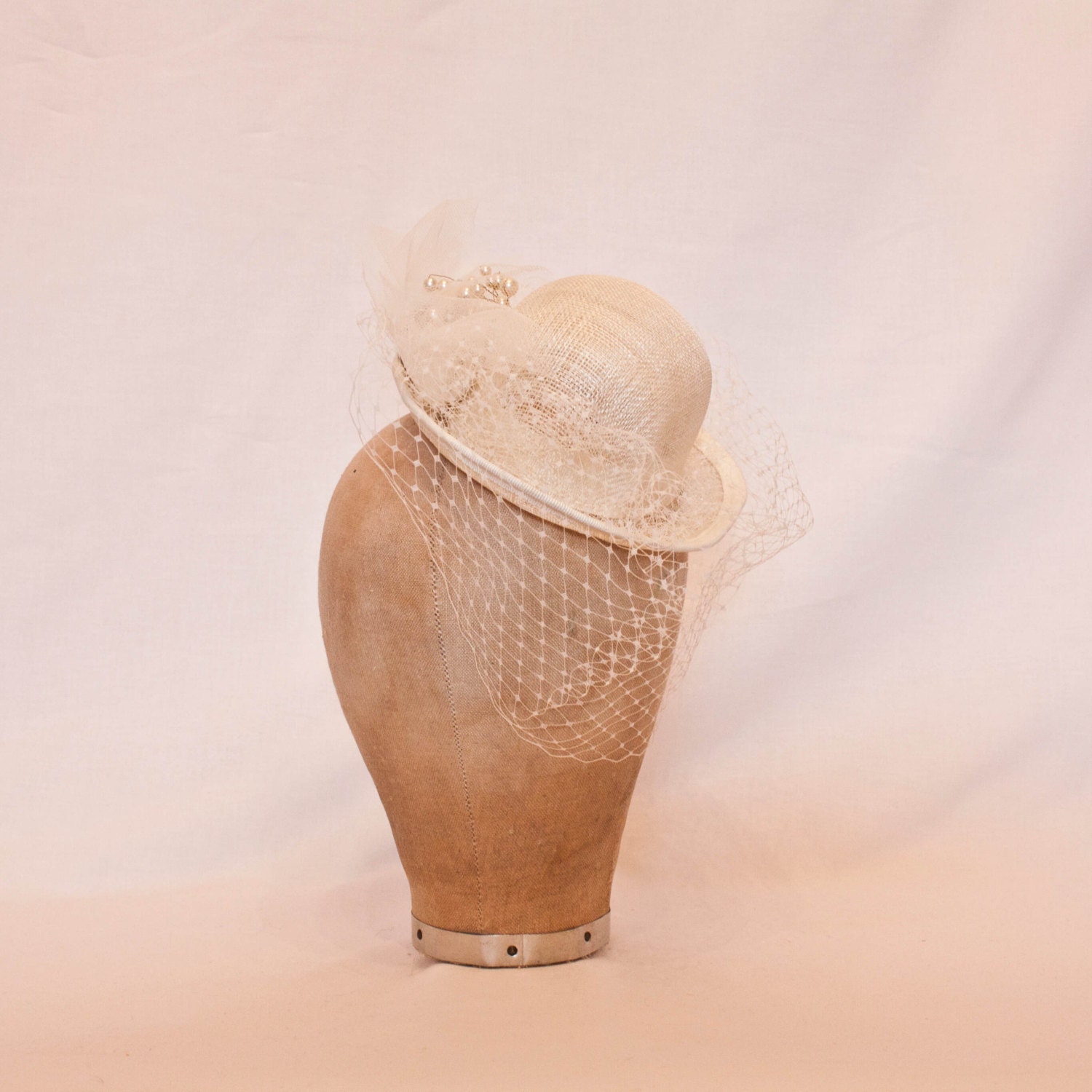 Small ivory bowler hat shaped fascinator with veiling and pearl bead detailing