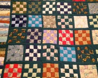 A true heirloom! Handstitched patchwork quilt with square block design in various colors borederd in green.