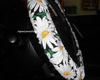 Steering wheel cover with large white daisies on black background with green leaves. Floral car accessories.