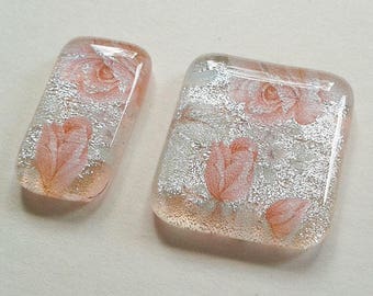 Pair of silver dichroic glass cabochons with pink rose patterns.
