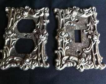 One Decorative Metal Light Switch Cover And One Outlet Cover Marked American Tack Hdwe Co 1967 and AT&HC