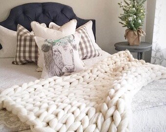 A person arm-knitting a blanket with friends in a cozy living room setting