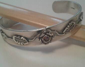 Fine silver cuff made with a red cz stone centered in the middle of a silver rose. Laminated rose and leaf motif.
