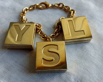 Super smart Yves Saint Laurent, French vintage charm bracelet, one lip gloss, one lipstick and one highlighter, hand bag / purse decor.