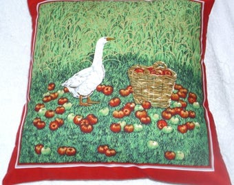 Goose in a corn field with rosy red apples in a basket cushion