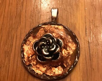pretty delicate silver rose flower set on top of bronze colored gold foil flakes in a round circle silver bezel about the size of a dime