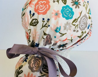 Ponytail Scrub Cap scrub hat featuring a beige material with flowers in peach teal and green with a coordinating band 2t