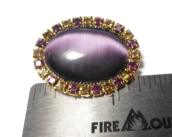 Marvella amethyst cat's eye brooch, Marvella by Monet oval purple glass cabochon surrounded by purple and amethyst frame, gold tone setting